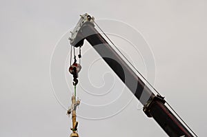 Construction crane with boom structure at construction site. The rise of the golden cross on the dome of the temple, gray cloudy