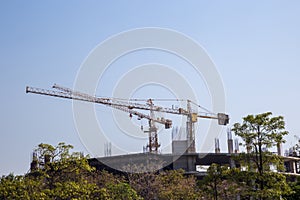 the construction crane and the building against the blue sky. Tower crane at the construction site against the blue sky.