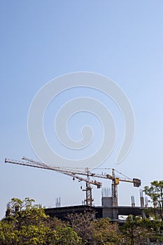 The construction crane and the building against the blue sky. Tower crane at the construction site against the blue sky.