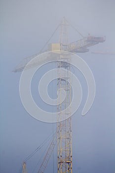 Construction crane in the fog on a sunny day