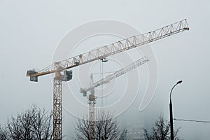 Construction crane, lantern and trees in the background of a house in the fog