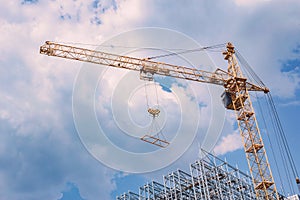 Construction crane with a new steel structure building. Against the background of a blue sky with clouds