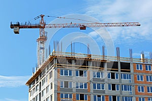 A construction crane is positioned at a building site, lifting materials to workers on a
