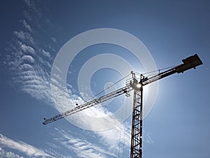 Construction crane silhouette with sun in blue sky with clouds
