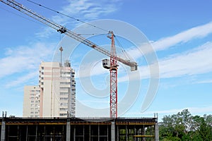 A construction crane is transporting a tool. Boom crane on the construction of a high-rise building. Blue sky, scaffolding