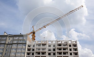 Construction crane on an unfinished residential building against the sun and blue sky. Housing construction, apartment building in