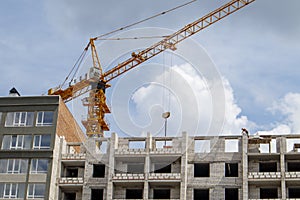 Construction crane on an unfinished residential building against the sun and blue sky. Housing construction, apartment building in