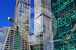 Construction cranes on the background of glass facades of skyscrapers in sunny day