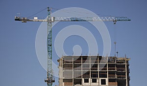 Construction cranes and high-rise building under construction against blue sky.