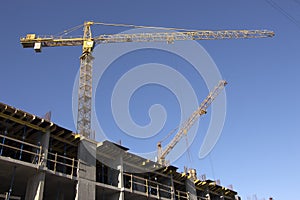 Construction cranes and high-rise building under construction against blue sky.