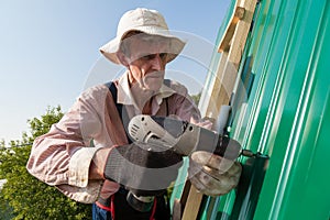 Construction elderly worker install new roof, Roofing tools, Electric drill used on new roofs with Metal Sheet. Self-made house by