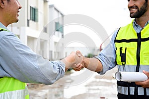 Construction engineer and architect with blueprint shaking hands while standing on construction site. Home building concept