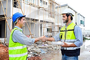 Construction engineer and architect with blueprint shaking hands while standing on construction site. Home building concept