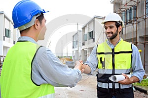 Construction engineer and architect with blueprint shaking hands while standing on construction site. Home building concept