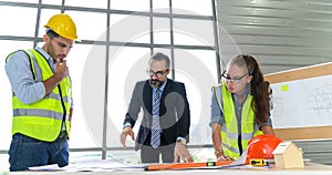 Construction engineer and architect in vest and helmet discussing blueprint with construction manager, standing on construction