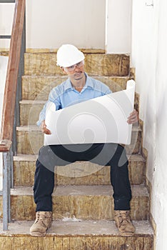 Construction engineer man hold blueprint wear blue shirt safety white hard hat at construction site industry labor worker.