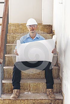 Construction engineer man hold blueprint wear blue shirt safety white hard hat at construction site industry labor worker.