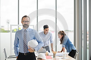 Construction engineer manager stand and holding white hardhat in front of engineers team meeting for architectural project