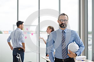 Construction engineer manager stand and holding white hardhat in front of engineers team meeting for architectural project