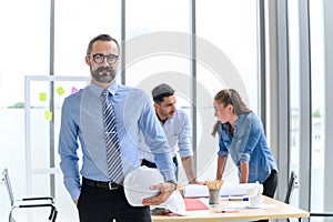 Construction engineer manager stand and holding white hardhat in front of engineers team meeting for architectural project