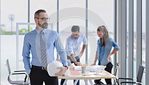 Construction engineer manager stand and holding white hardhat in front of engineers team meeting for architectural project in the