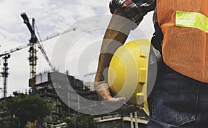 The construction engineer is watching the work and holding a yellow safety helmet