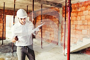 Construction engineer working on house building site - reading paper plans and coordinating workers