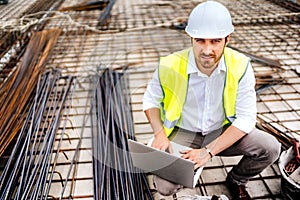 construction engineer working on laptop, wearing safety equipement and coordinating workers