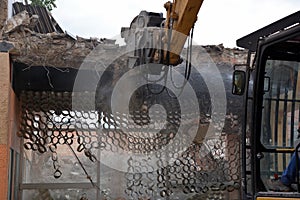 A construction excavator is engaged in the dismantling of an old brick house