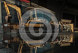 Construction excavator of yellow color and Old waters pumps with reflection on water