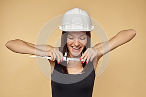 Construction girl in a white hard hat and protective construction mask holding a caliper. makes the measurement of the smile