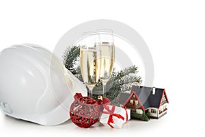 Construction hard hat, fir tree branches, model house, two glasses with champange and Christmas ornament isolated on a white