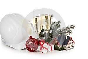 Construction hard hat, fir tree branches, model house, two glasses with champange and Christmas ornament isolated on a white