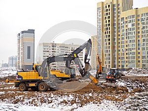 Construction of high-rise buildings in winter. The work of excavators. Land works. Digging pits. Concrete building frames