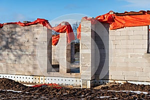 Construction of a house stopped for the winter. The top of the building covered in orange plastic sheeting. Frozen ground with