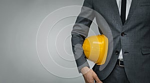 Construction industry business - businessman holding yellow hard hat underarm on gray background photo