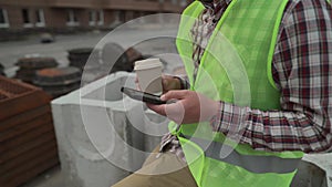 Construction industry worker texting during lunch break. Helmeted handyman chatting and using smartphone during coffee