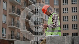 Construction industry worker texting during lunch break. Helmeted handyman chatting and using smartphone during coffee