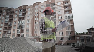 Construction inspector with blueprints on building site. Engineer in protective workwear checking technical design