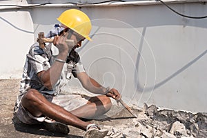 A construction labour working with hammer and Chisel wearing safety helmet in a construction site