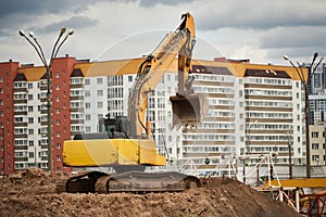 construction machine excavator standing in front of modern apartment building. Real estate development