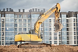 construction machine excavator standing in front of modern apartment building. Real estate development