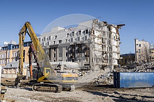 Construction machines near multi-storey building without walls and bare load-bearing structures, gradually destroyed for