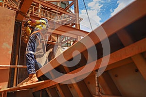 Construction maintenance worker wearing safety helmet, fall arrest harness clipping while working at height