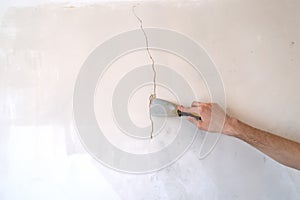 Construction man worker repairing a crack wall of a home, plastering cement on wall. Builder applying white cement to a