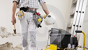 Construction man worker wearing a tool bag belt, helmet with headphones and hammer in his hands, gloves in your pocket, compressor