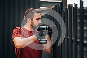 Construction man working with screwdriver on metal fence