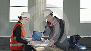 Construction manager female architect and consultant welder in protective helmets discuss new hangar project