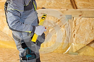 Construction mason worker with building level and screwdriver on attic with environmentally friendly