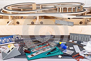 Construction of model railroad with wooden open frame layout. workbench with model railway train station and landscape tools.